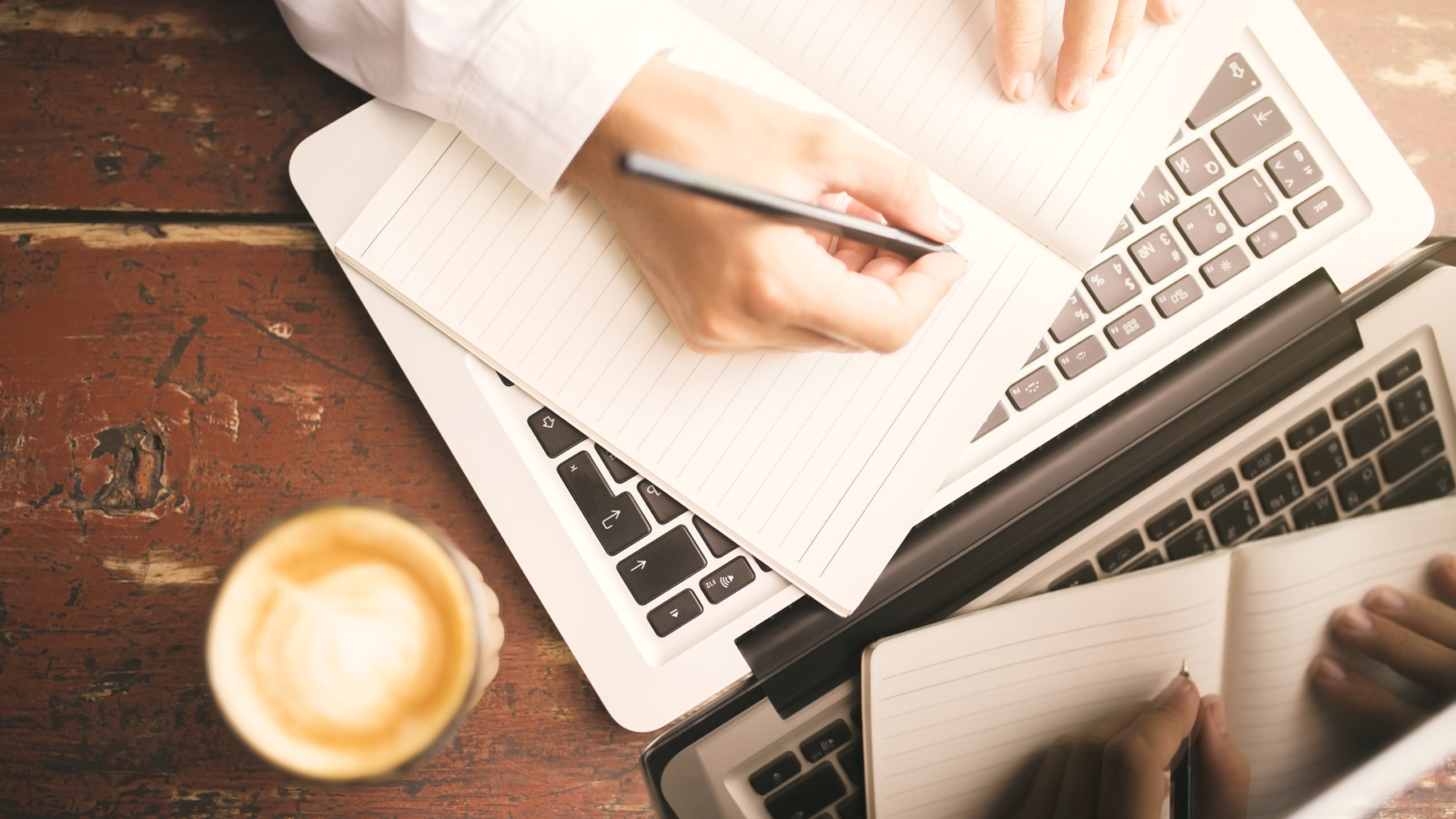 Man hands writing in the diary, coffee mug and laptop on wooden table