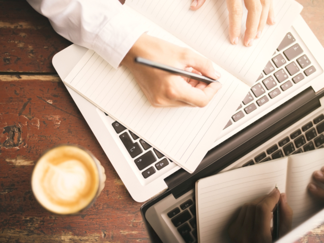 Man hands writing in the diary, coffee mug and laptop on wooden table